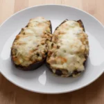Un plato con dos berenjenas rellenas de carne y tomate gratinadas al horno