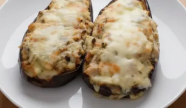Un plato con dos berenjenas rellenas de carne y tomate gratinadas al horno