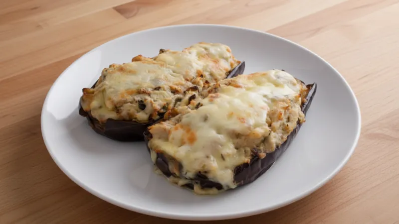 Dos berenjenas rellenas de carne y tomate gratinadas al horno sobre un plato blanco.