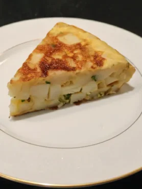 Un trozo de tortilla de patatas con cebolla y perejil en un plato blanco