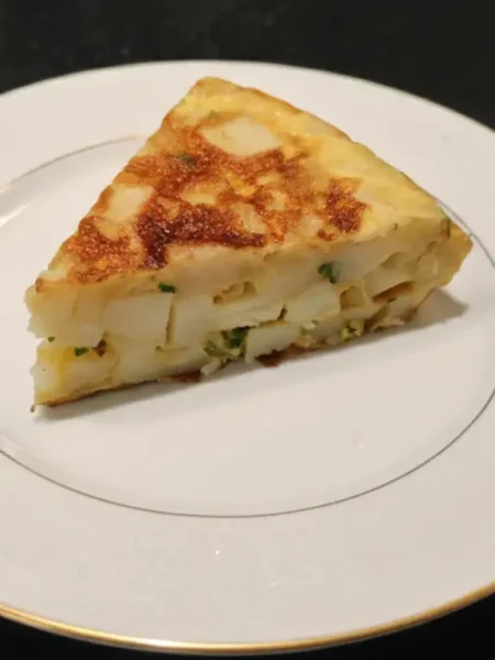Un trozo de tortilla de patatas con cebolla y perejil en un plato blanco