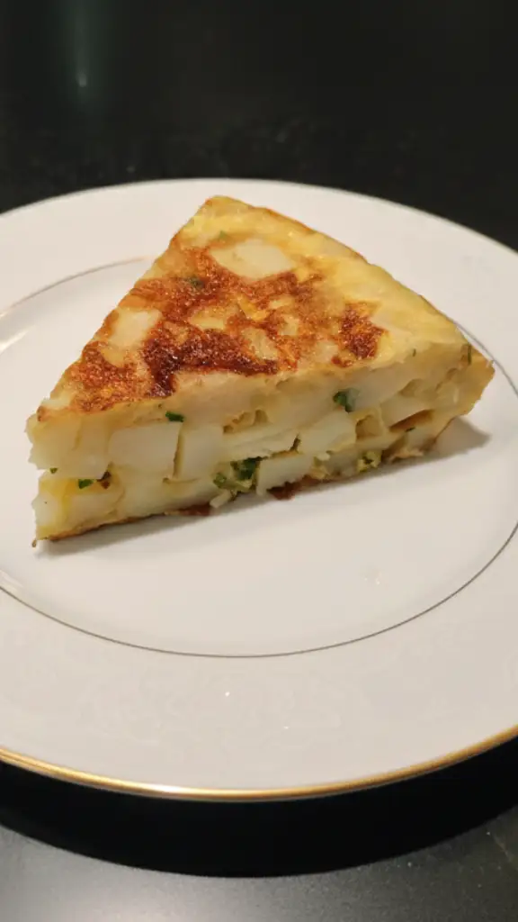 Un trozo de tortilla de patatas con cebolla y perejil en un plato blanco