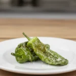 Dos pimientos de padrón fritos en un plato sobre una mesa