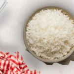 Un cuenco con arroz blanco básico con ajo y laurel junto a un paño de cocina y una ristra de ajos.