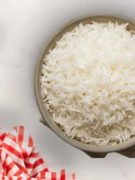 Un cuenco con arroz blanco básico con ajo y laurel junto a un paño de cocina y una ristra de ajos.