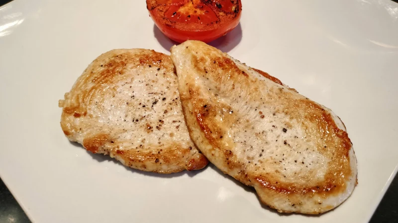 Un plato con pechuga de pollo a la plancha y tomate asado