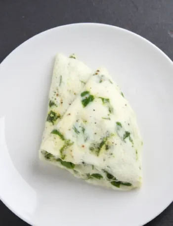 Una tortilla de claras con espinacas partida en dos sobre un plato blanco