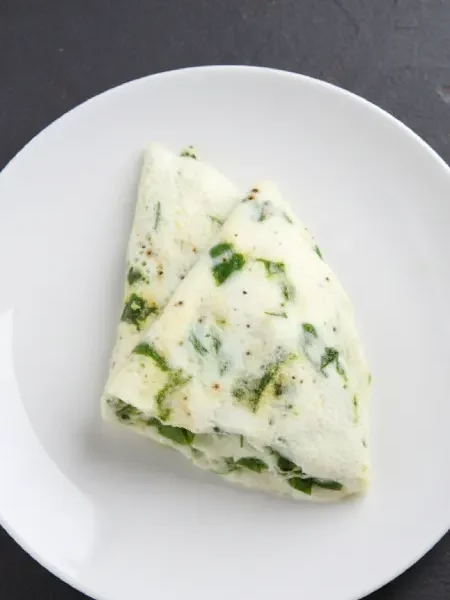 Una tortilla de claras con espinacas partida en dos sobre un plato blanco